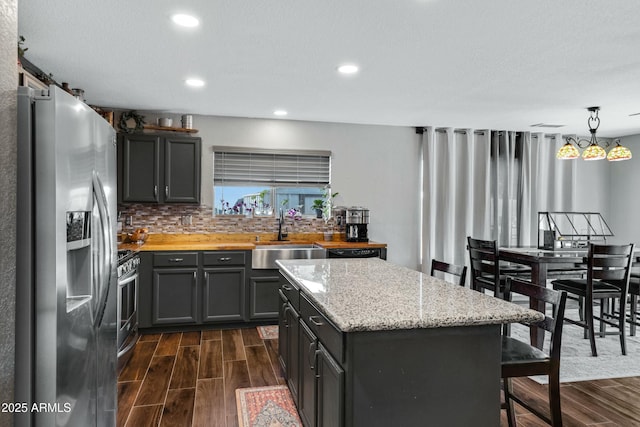 kitchen with sink, appliances with stainless steel finishes, hanging light fixtures, a center island, and light stone counters