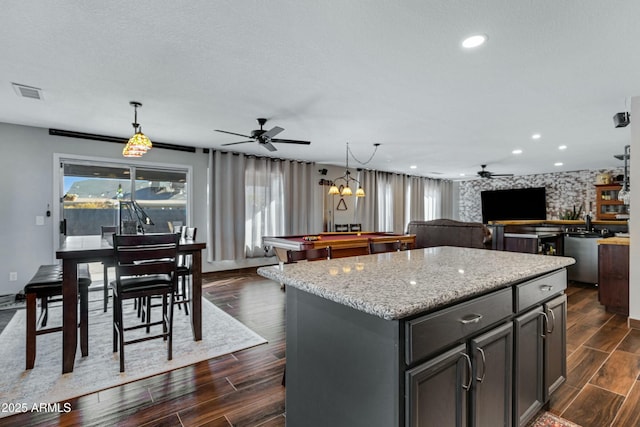 kitchen with gray cabinets, a kitchen island, decorative light fixtures, light stone counters, and a textured ceiling