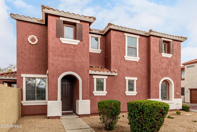 mediterranean / spanish-style house featuring stucco siding, a tile roof, and fence