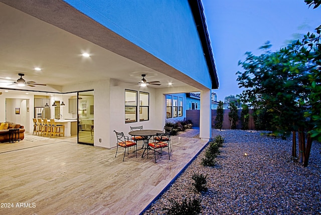 patio terrace at dusk featuring ceiling fan and exterior bar