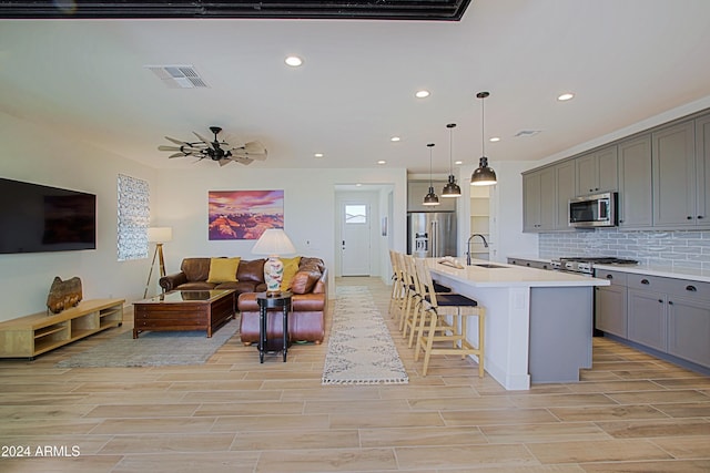 kitchen with hanging light fixtures, decorative backsplash, gray cabinets, an island with sink, and stainless steel appliances