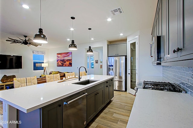 kitchen featuring light wood-type flooring, stainless steel appliances, sink, decorative light fixtures, and an island with sink