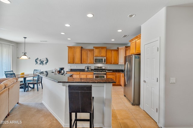 kitchen featuring light tile patterned flooring, appliances with stainless steel finishes, an island with sink, a kitchen bar, and hanging light fixtures