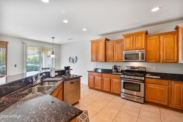 kitchen featuring sink, light tile patterned floors, appliances with stainless steel finishes, dark stone countertops, and hanging light fixtures