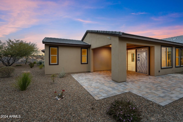 back house at dusk featuring a patio area