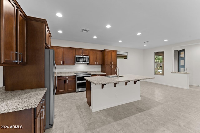 kitchen with light stone countertops, sink, stainless steel appliances, a breakfast bar area, and a kitchen island with sink