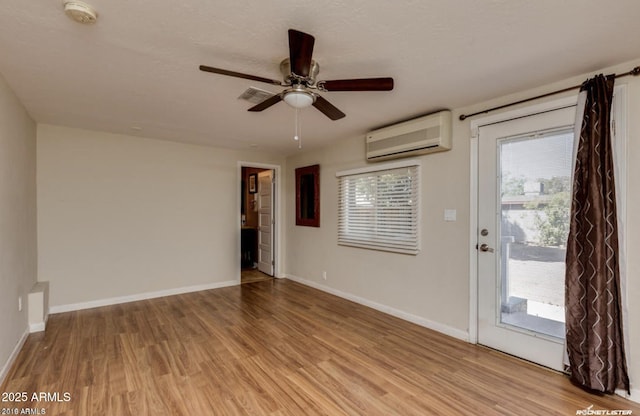 unfurnished room with ceiling fan, a wall unit AC, and light hardwood / wood-style flooring