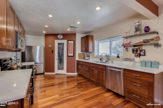 kitchen featuring sink, light wood-type flooring, a textured ceiling, and appliances with stainless steel finishes