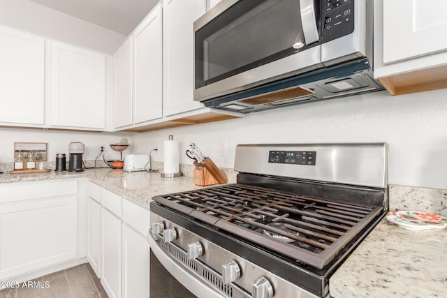 kitchen featuring white cabinetry, light stone countertops, stainless steel appliances, and light hardwood / wood-style floors