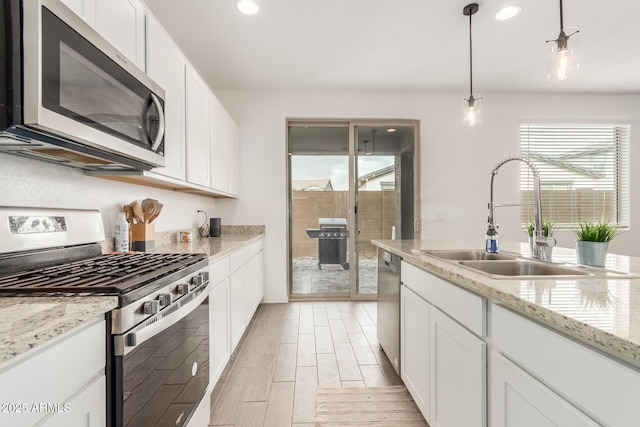 kitchen featuring sink, appliances with stainless steel finishes, white cabinetry, a healthy amount of sunlight, and decorative light fixtures