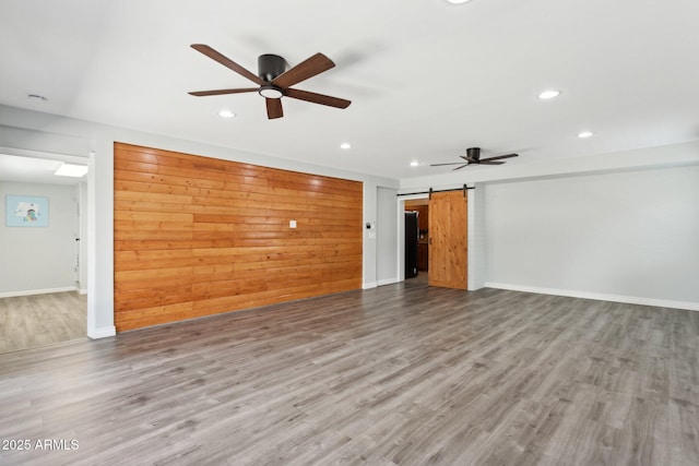 unfurnished living room featuring a ceiling fan, recessed lighting, wood finished floors, a barn door, and baseboards