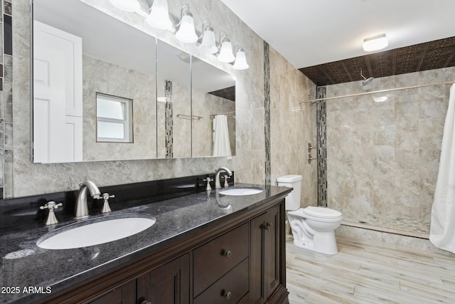 bathroom featuring a shower stall, tile walls, toilet, double vanity, and wood finished floors
