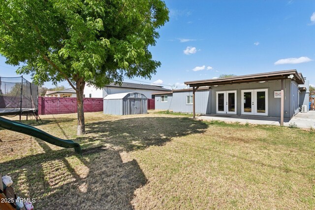 rear view of house with french doors, a trampoline, a storage shed, and an outbuilding