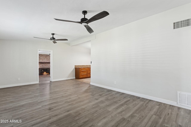 unfurnished living room with wood finished floors, a ceiling fan, a brick fireplace, and baseboards