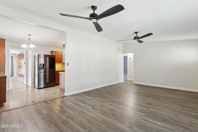 unfurnished living room with ceiling fan, a chandelier, wood finished floors, and baseboards