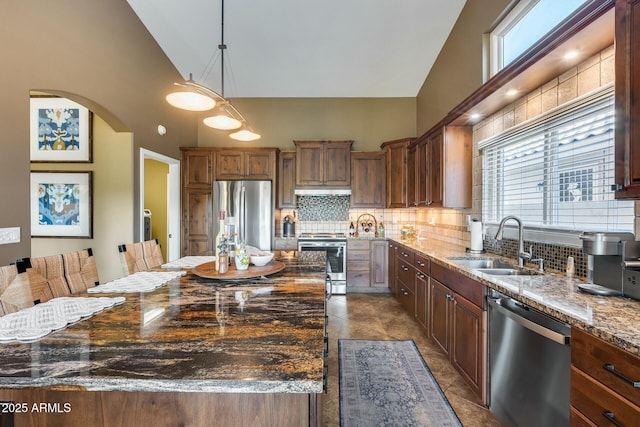 kitchen with pendant lighting, sink, dark stone countertops, stainless steel appliances, and a center island