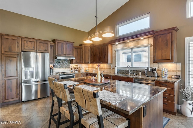 kitchen featuring sink, a center island, appliances with stainless steel finishes, pendant lighting, and dark stone counters