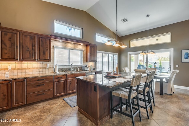 kitchen with a breakfast bar, pendant lighting, sink, dark stone countertops, and a center island