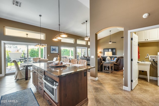 kitchen with high vaulted ceiling, a center island, decorative light fixtures, oven, and dark stone counters