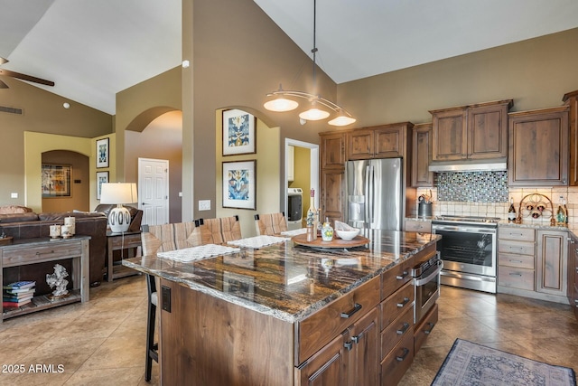 kitchen featuring dark stone countertops, a kitchen island, a kitchen breakfast bar, and appliances with stainless steel finishes