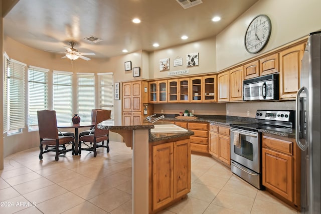 kitchen with light tile patterned floors, stainless steel appliances, ceiling fan, a center island with sink, and sink