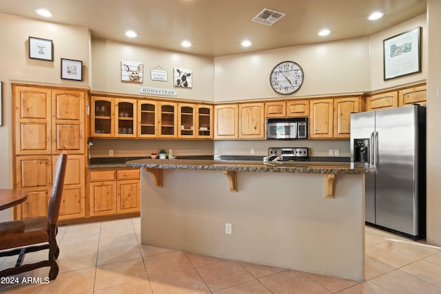 kitchen with light tile patterned flooring, an island with sink, a kitchen bar, appliances with stainless steel finishes, and a high ceiling