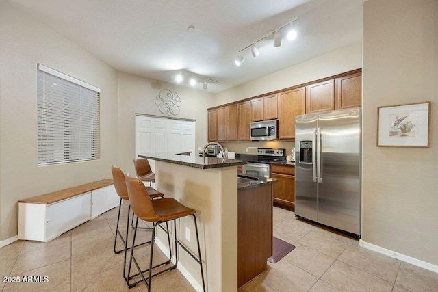 3330 S Gilbert Rd Unit 2090, Chandler, AZ 85286 - kitchen featuring an island with sink, a kitchen breakfast bar, appliances with stainless steel finishes, brown cabinetry, and light tile patterned floors