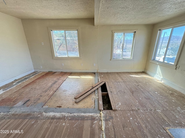 unfurnished room featuring a textured ceiling, wood-type flooring, and baseboards