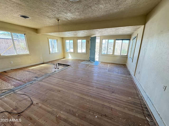 unfurnished living room with wood-type flooring, visible vents, a textured wall, and a textured ceiling