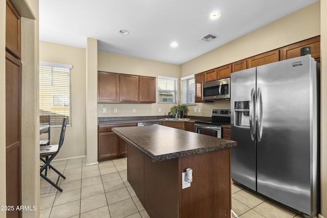 2111 N 77th Gln, Phoenix, AZ 85035 - kitchen with stainless steel appliances, dark countertops, light tile patterned floors, a center island, and recessed lighting
