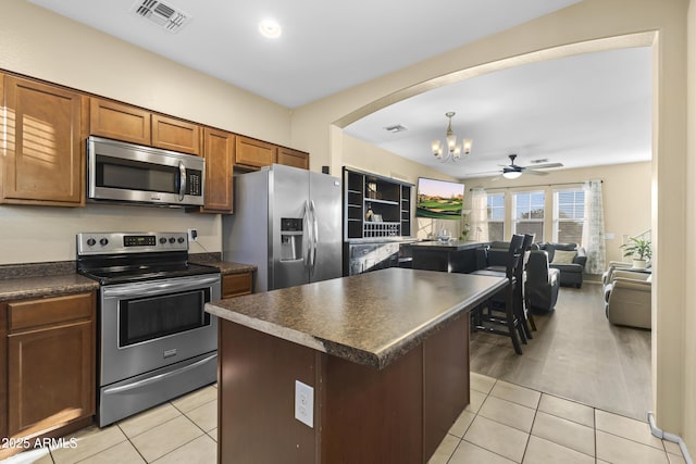 2111 N 77th Gln, Phoenix, AZ 85035 - kitchen with stainless steel appliances, dark countertops, a chandelier, arched walkways, and brown cabinets