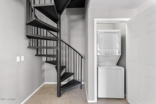 laundry area featuring stacked washing maching and dryer, light tile patterned floors, and baseboards