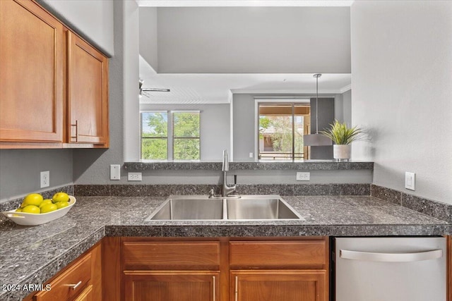 kitchen with brown cabinetry, dark countertops, a sink, and stainless steel dishwasher