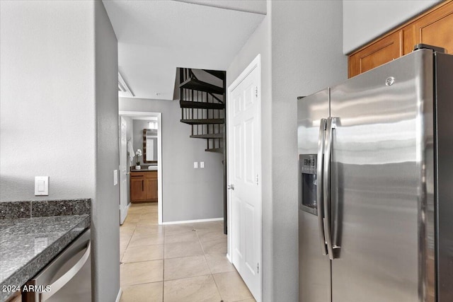 kitchen featuring light tile patterned floors, baseboards, brown cabinetry, dark countertops, and appliances with stainless steel finishes