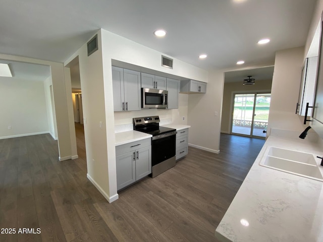 kitchen featuring gray cabinetry, stainless steel appliances, light stone countertops, dark wood-type flooring, and sink