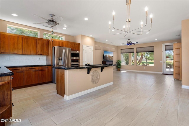 kitchen with tasteful backsplash, a center island, stainless steel appliances, and ceiling fan with notable chandelier