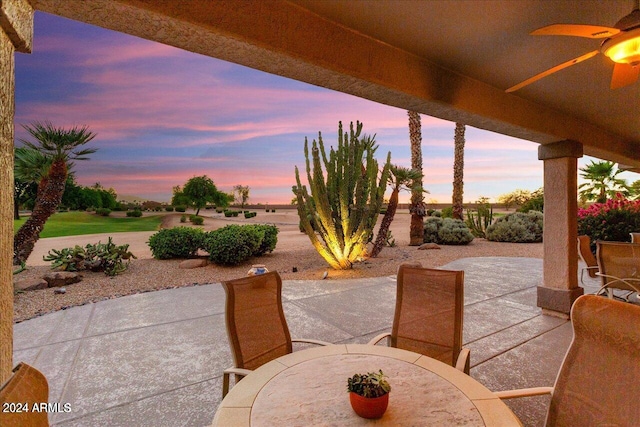 patio terrace at dusk featuring a water view and ceiling fan