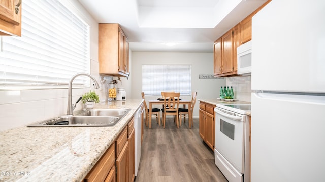 kitchen featuring white appliances, light wood finished floors, a tray ceiling, a sink, and backsplash