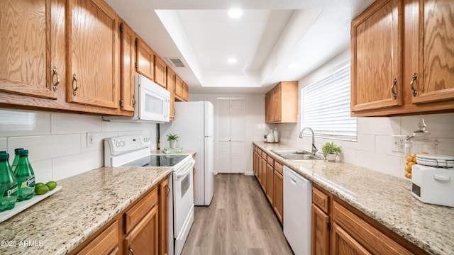 kitchen with visible vents, a tray ceiling, light wood-style flooring, white appliances, and a sink