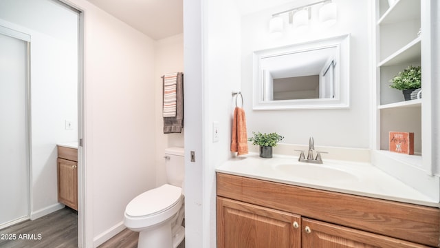 bathroom featuring toilet, vanity, baseboards, and wood finished floors