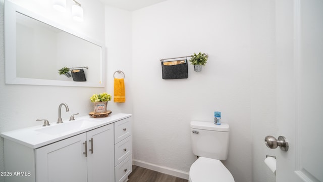 half bathroom featuring toilet, vanity, baseboards, and wood finished floors