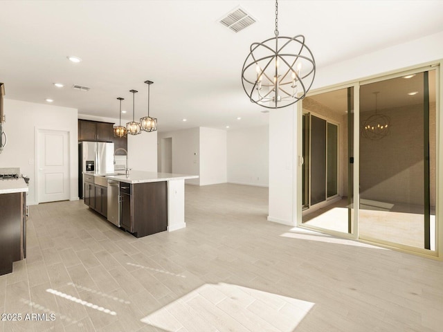 kitchen with dark brown cabinetry, hanging light fixtures, dishwasher, an island with sink, and a notable chandelier