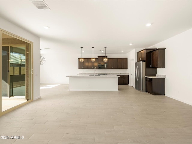 kitchen featuring dark brown cabinetry, sink, decorative light fixtures, stainless steel appliances, and a kitchen island with sink