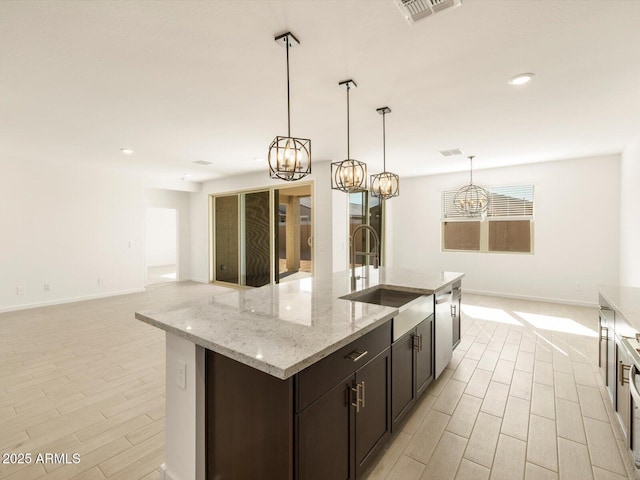 kitchen featuring pendant lighting, sink, a kitchen island with sink, dark brown cabinetry, and light stone counters