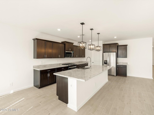 kitchen with sink, decorative light fixtures, a center island with sink, appliances with stainless steel finishes, and light stone countertops