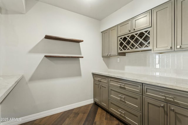 kitchen with light stone countertops, dark hardwood / wood-style floors, gray cabinetry, and backsplash