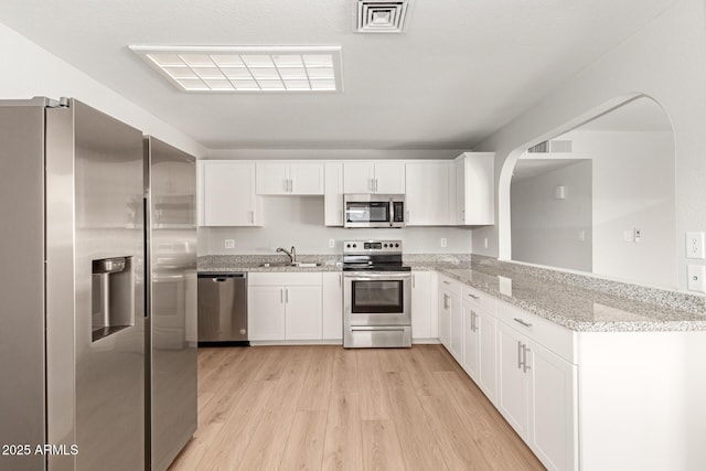 kitchen with light stone countertops, white cabinets, appliances with stainless steel finishes, sink, and kitchen peninsula