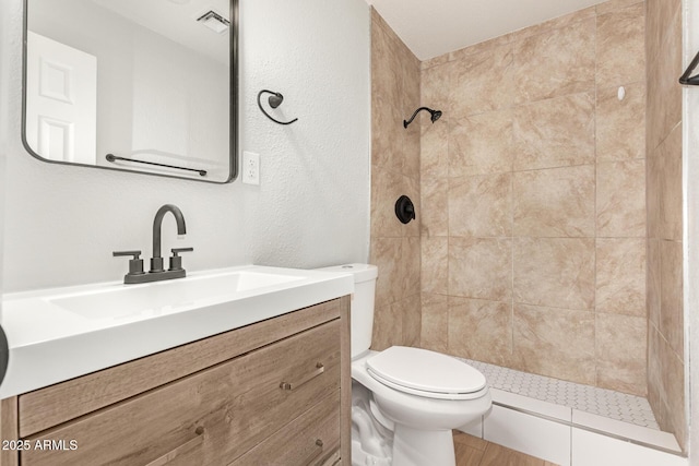 bathroom featuring a tile shower, toilet, and vanity