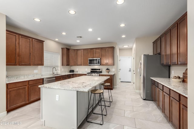 kitchen featuring light stone countertops, a kitchen breakfast bar, stainless steel appliances, light tile patterned floors, and a kitchen island