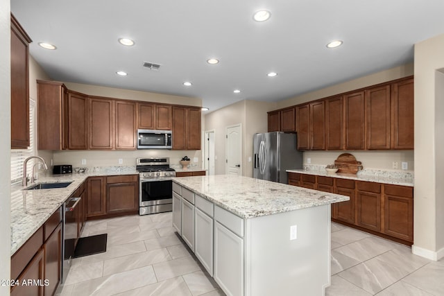 kitchen with a center island, stainless steel appliances, light stone counters, and sink